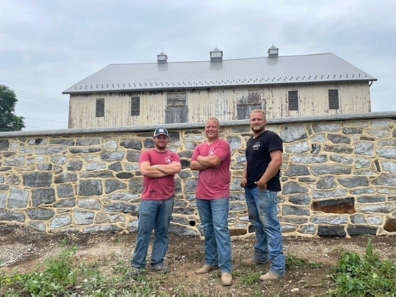 The Poor Boys' Enterprises crew standing in front of a restored stone bank barn