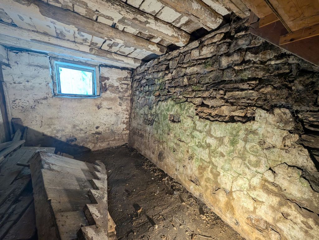 Deteriorated stone barn foundation with moss and eroded mortar before repair